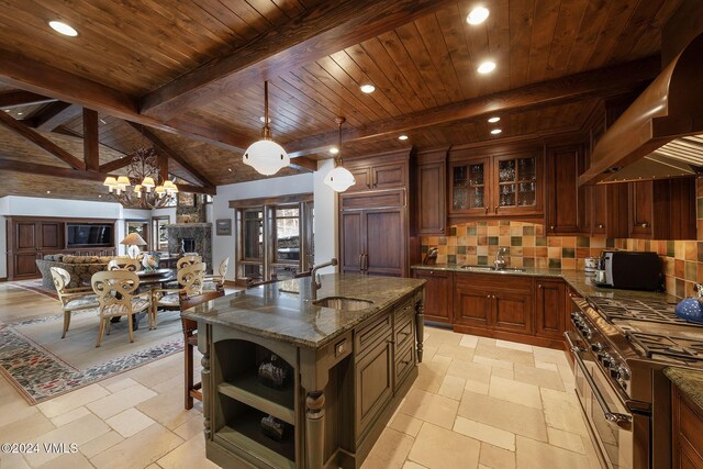 kitchen featuring a center island with sink, premium appliances, wall chimney exhaust hood, glass insert cabinets, and a sink