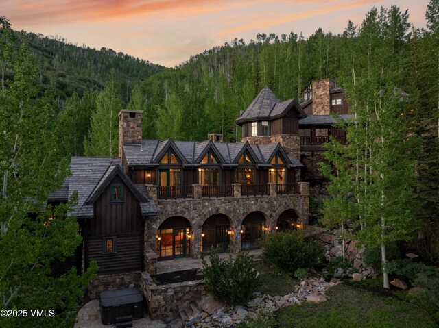 1094 Riva Gln, Vail, CO 81657 - view of front of property with stone siding, a balcony, a chimney, and a view of trees