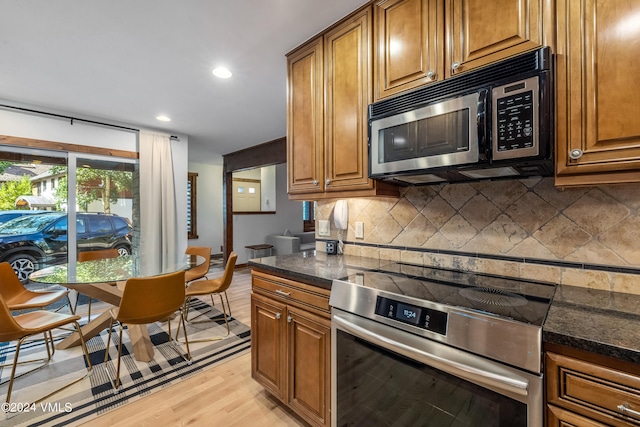 kitchen featuring range with electric cooktop, light wood-type flooring, tasteful backsplash, and dark stone countertops