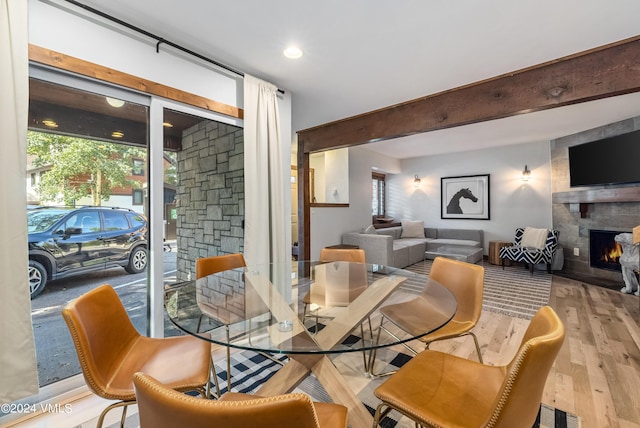 dining space featuring beam ceiling, plenty of natural light, a large fireplace, and light hardwood / wood-style floors