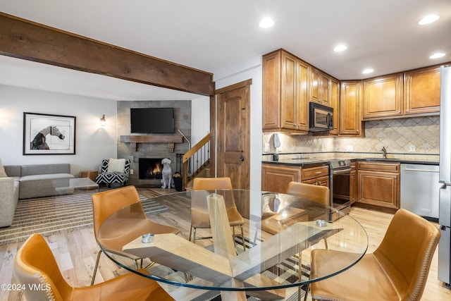 dining area with sink, a fireplace, beamed ceiling, and light wood-type flooring