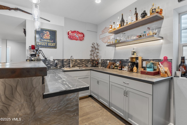 bar featuring sink, gray cabinetry, light wood-type flooring, and decorative backsplash