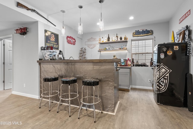 bar with hanging light fixtures, black refrigerator, and light hardwood / wood-style floors