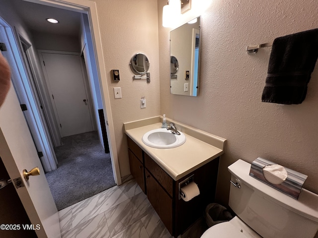 bathroom with marble finish floor, a textured wall, vanity, and toilet