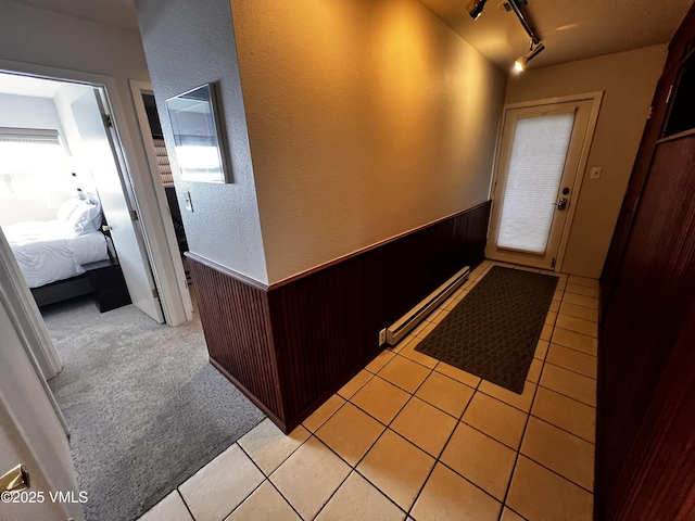 interior space featuring light tile patterned floors, wooden walls, wainscoting, a baseboard radiator, and rail lighting