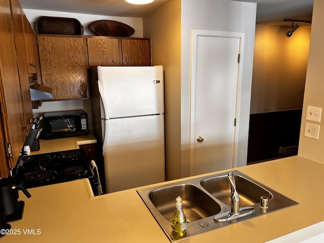 kitchen featuring freestanding refrigerator, light countertops, a sink, and electric range oven