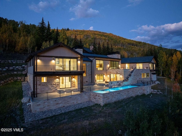 1326 Spraddle Creek Rd, Vail, CO 81657 - back of house with a balcony, a forest view, stone siding, a chimney, and a patio area