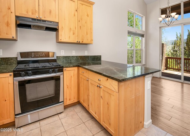 kitchen featuring stainless steel gas range, under cabinet range hood, a peninsula, light brown cabinets, and a chandelier