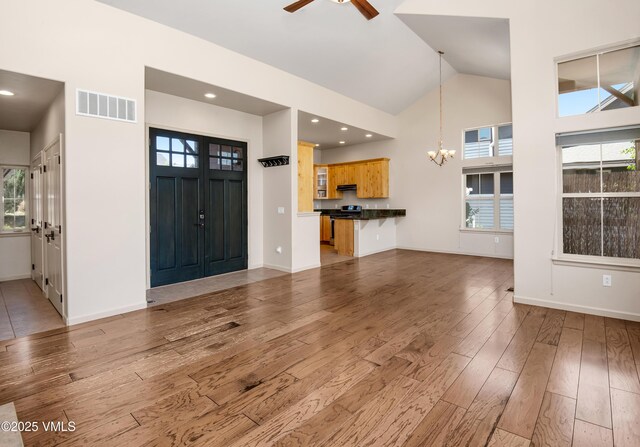 unfurnished living room with a chandelier, light wood-style floors, ceiling fan, high vaulted ceiling, and healthy amount of natural light