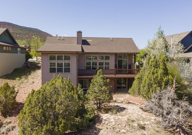 back of property with a deck, a chimney, and a shingled roof