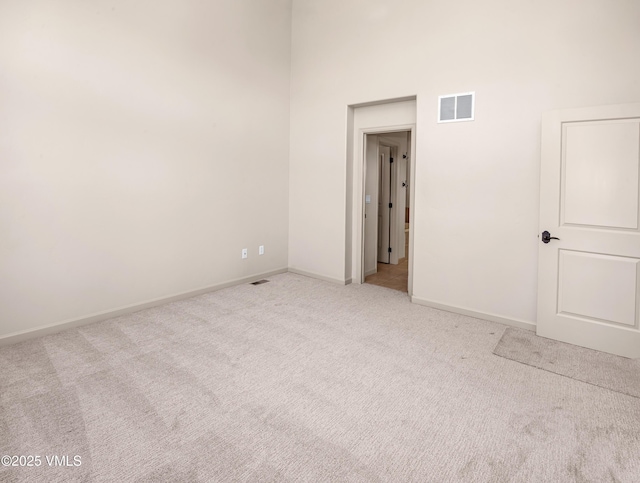 unfurnished room featuring light colored carpet, a high ceiling, and baseboards