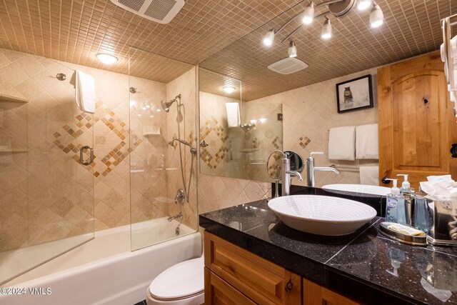 full bathroom featuring vanity, combined bath / shower with glass door, tile walls, and toilet