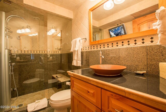 bathroom with toilet, a shower with shower door, tile walls, vanity, and backsplash