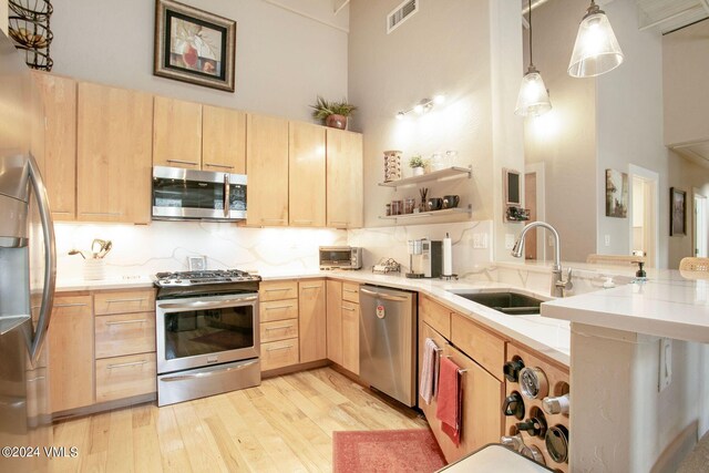 kitchen with sink, light brown cabinets, appliances with stainless steel finishes, pendant lighting, and a towering ceiling