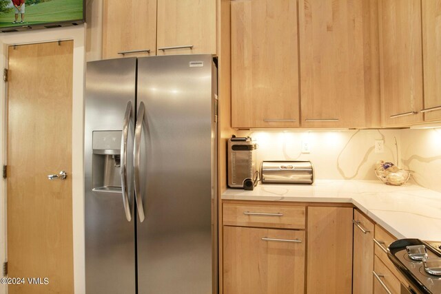 kitchen with stainless steel fridge with ice dispenser, cooktop, and light brown cabinets