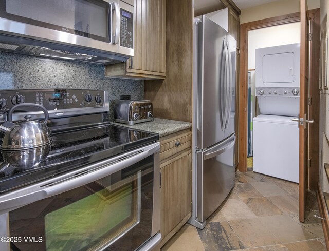 kitchen featuring appliances with stainless steel finishes, stacked washer / dryer, and backsplash