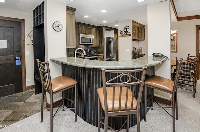 kitchen featuring tasteful backsplash, a kitchen breakfast bar, kitchen peninsula, stainless steel appliances, and a textured ceiling