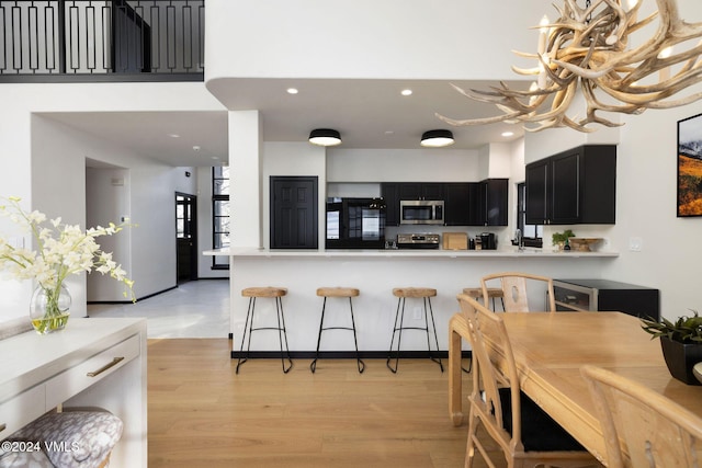 kitchen with appliances with stainless steel finishes, a notable chandelier, light hardwood / wood-style floors, a kitchen bar, and kitchen peninsula