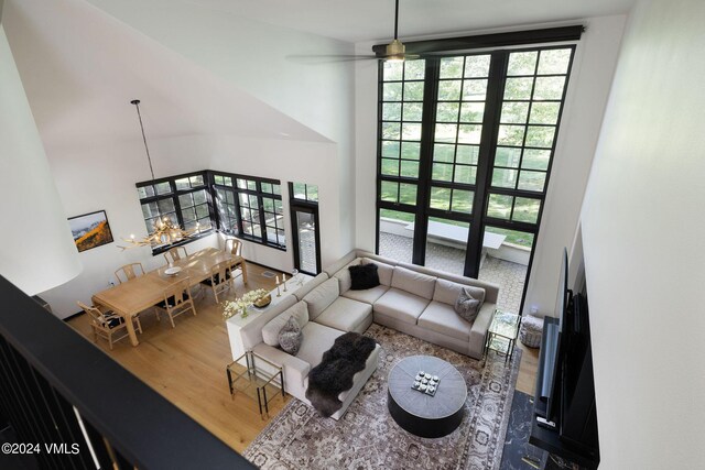 living room with hardwood / wood-style flooring, ceiling fan with notable chandelier, and a high ceiling