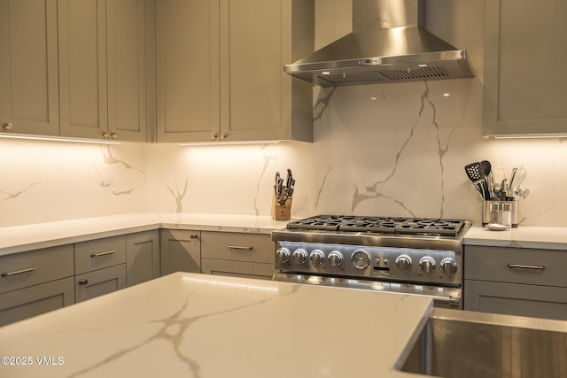 kitchen with gray cabinetry, light stone counters, exhaust hood, stainless steel range, and backsplash