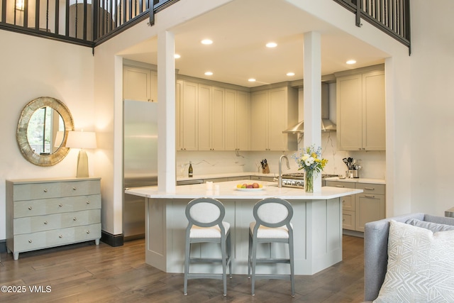 kitchen featuring a kitchen island with sink, dark wood-type flooring, a breakfast bar area, and wall chimney exhaust hood