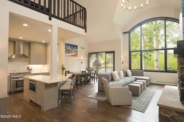 living room with an inviting chandelier, a towering ceiling, dark hardwood / wood-style floors, and baseboard heating