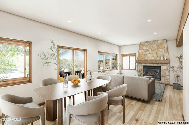 dining room featuring a wealth of natural light, light hardwood / wood-style flooring, and a stone fireplace