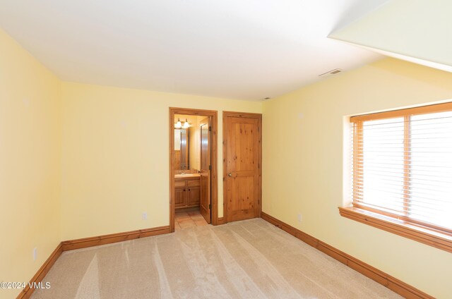 unfurnished bedroom featuring ensuite bathroom and light carpet