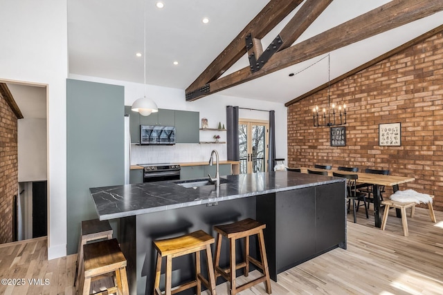 kitchen with beam ceiling, stainless steel appliances, dark countertops, light wood-style floors, and a sink