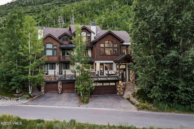 2417 Garmisch Dr Unit B, Vail, CO 81657 - craftsman-style home with an attached garage, driveway, a wooded view, stairs, and a chimney