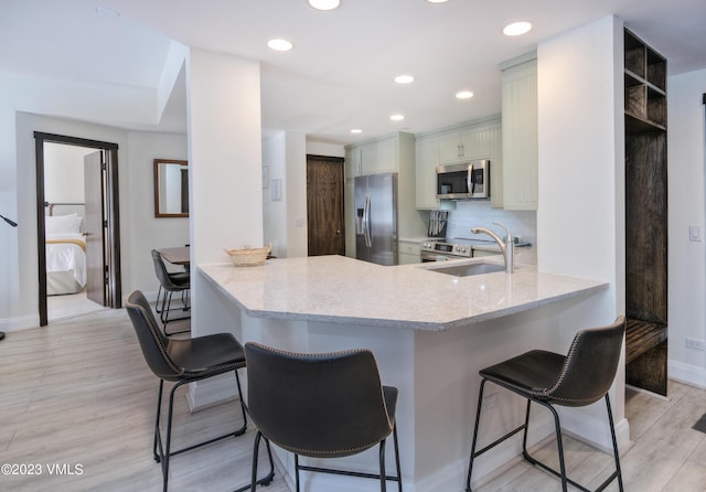 kitchen featuring sink, a kitchen breakfast bar, kitchen peninsula, stainless steel appliances, and backsplash