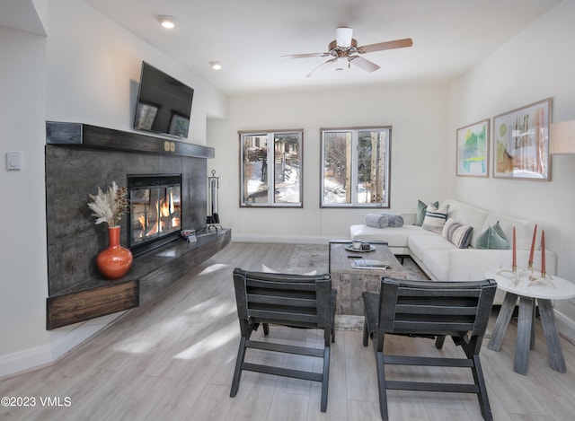 living room with a tiled fireplace, light hardwood / wood-style floors, and ceiling fan