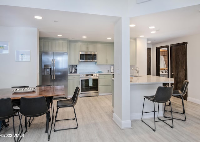 kitchen featuring tasteful backsplash, appliances with stainless steel finishes, kitchen peninsula, and light hardwood / wood-style flooring