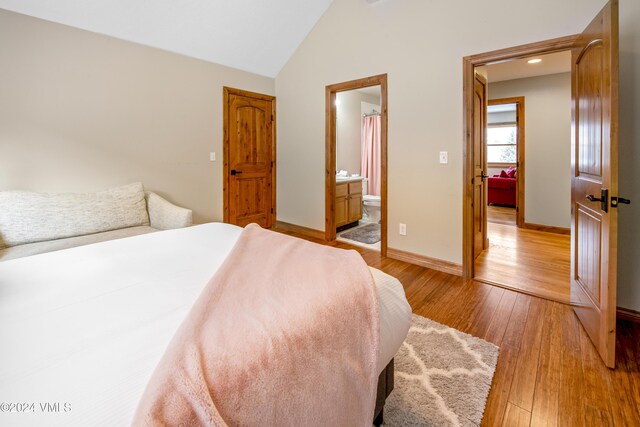 bedroom featuring connected bathroom, light hardwood / wood-style floors, and vaulted ceiling