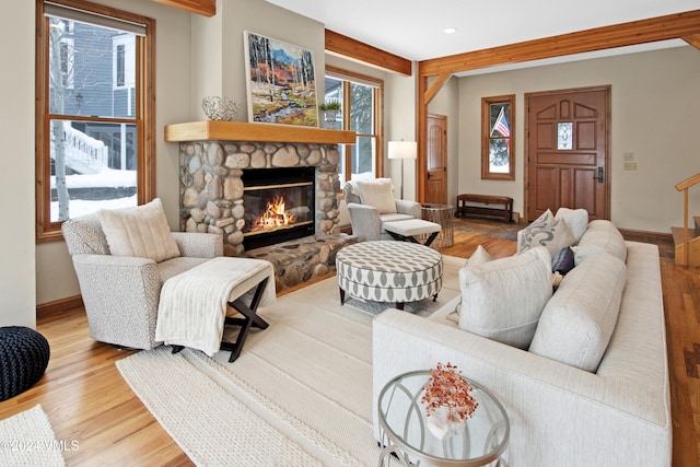 living room featuring beamed ceiling, a stone fireplace, and light wood-type flooring