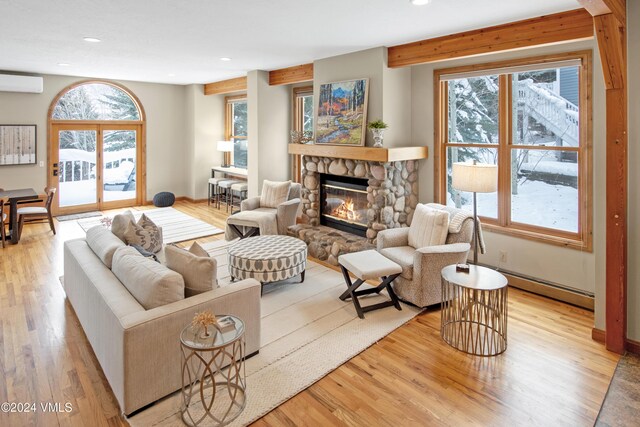 living room with a stone fireplace, a wall unit AC, and a wealth of natural light