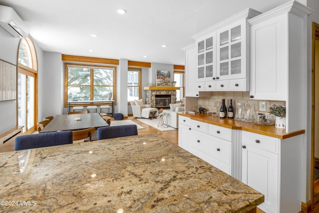 kitchen featuring white cabinetry, a stone fireplace, butcher block countertops, and an AC wall unit