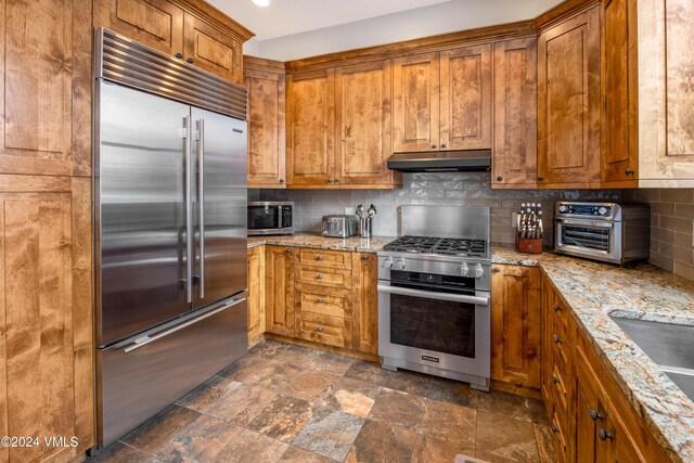 kitchen with high end appliances, tasteful backsplash, sink, and light stone counters