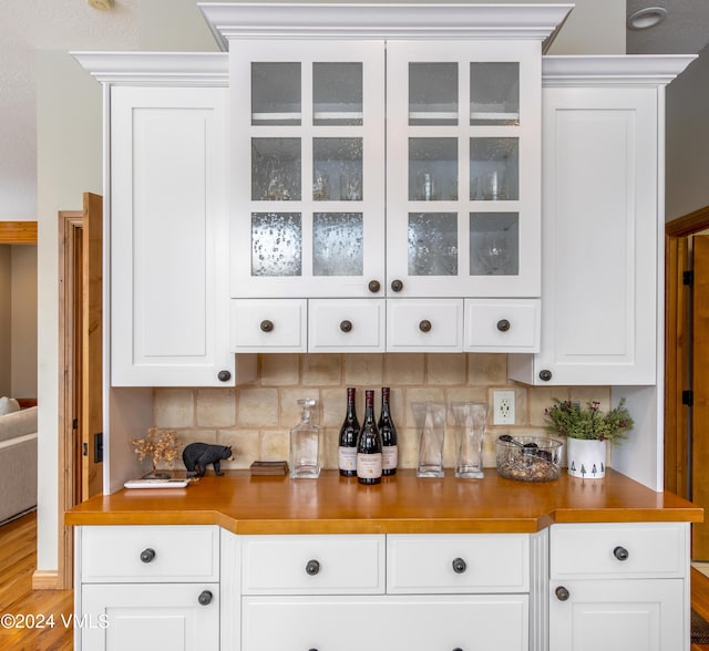 bar with white cabinets, light hardwood / wood-style flooring, and backsplash