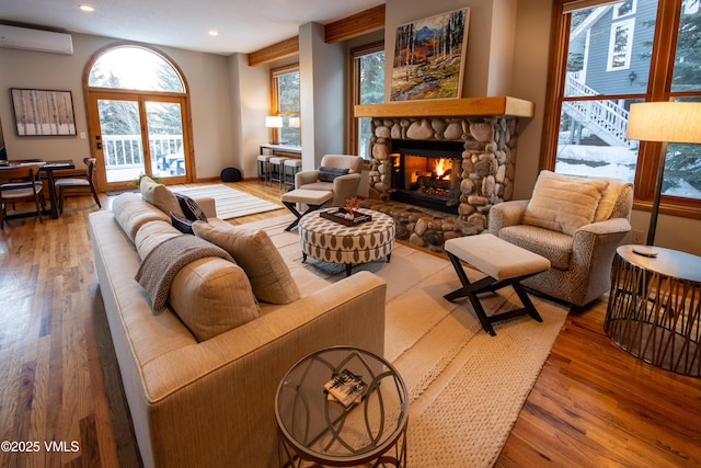 living room featuring wood-type flooring, an AC wall unit, and a stone fireplace