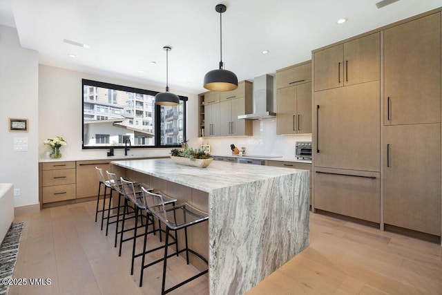 42 Riverfront Ln Unit Th-13, Avon, CO 81620 - kitchen featuring wall chimney exhaust hood, a breakfast bar, light wood-style floors, a center island, and light stone counters