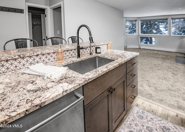 kitchen with sink, stainless steel dishwasher, light stone counters, dark brown cabinets, and light carpet