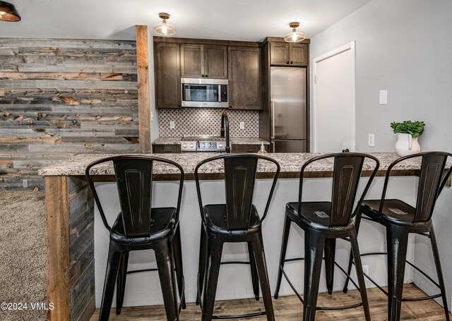 kitchen featuring dark brown cabinetry, decorative backsplash, a breakfast bar, and appliances with stainless steel finishes