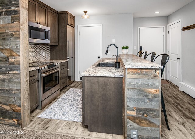 kitchen featuring sink, dark brown cabinets, a center island with sink, light wood-type flooring, and appliances with stainless steel finishes