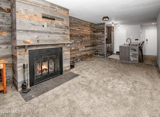 unfurnished living room featuring sink, a fireplace, wooden walls, and carpet flooring