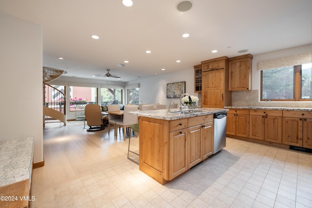 kitchen with sink, dishwasher, light stone counters, a healthy amount of sunlight, and a center island with sink