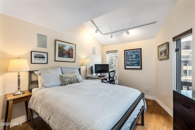 bedroom with track lighting, lofted ceiling, dark wood-type flooring, and baseboards