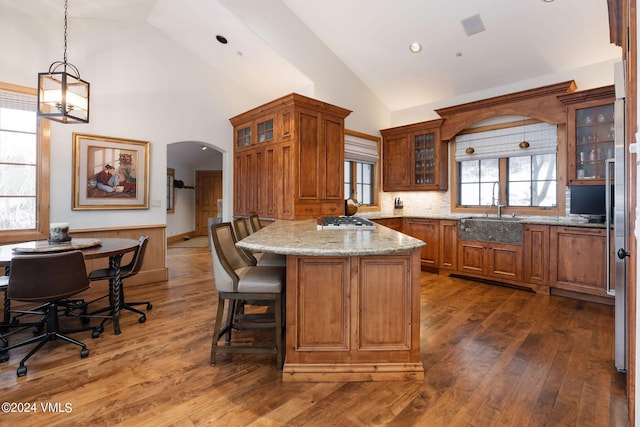 kitchen with sink, dark hardwood / wood-style floors, light stone countertops, stainless steel gas cooktop, and decorative light fixtures