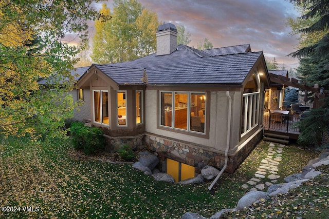 back house at dusk featuring a wooden deck and a lawn