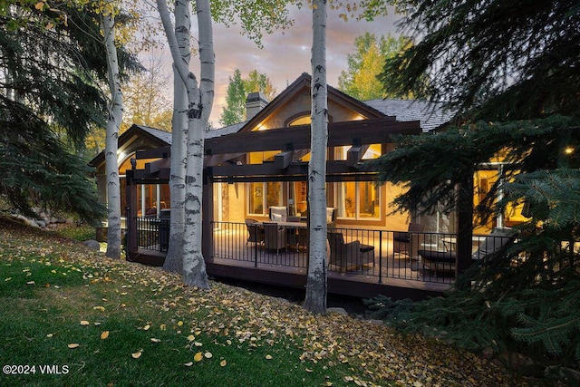 back house at dusk with a deck and a lawn